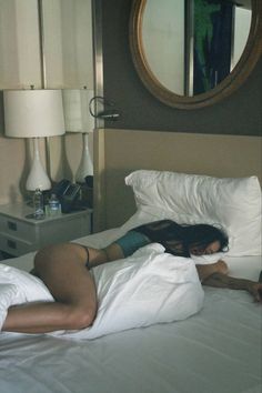 a woman laying on top of a white bed in a bedroom next to a mirror