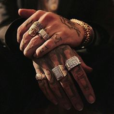 two hands holding each other with tattoos on their fingers and wearing gold rings, bracelets and necklaces