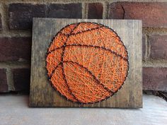 an orange and black string art piece on a wooden block with brick wall in the background