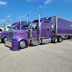 three purple semi trucks parked in a parking lot with blue sky and clouds behind them