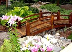 a wooden bridge with flowers and rocks in the foreground, surrounded by greenery