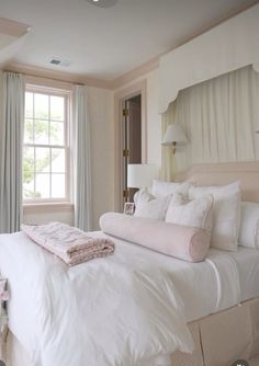 a white bed sitting in a bedroom next to a window with curtains on both sides