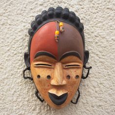 a wooden mask mounted to the side of a white wall with beads hanging from it's sides