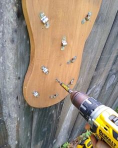 a person holding a drill and screwdriver next to a wooden board with nails on it