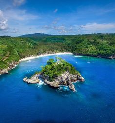 an island in the middle of blue water surrounded by lush green hills and trees on both sides