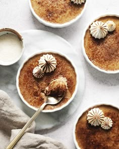 three bowls filled with dessert sitting on top of a white table next to spoons