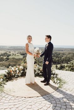 a bride and groom standing in front of an arch with white flowers on it at their wedding