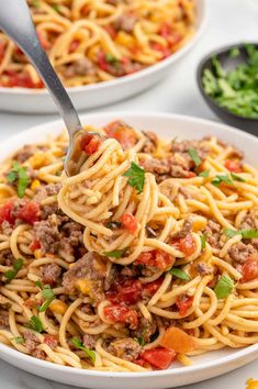 two bowls of spaghetti with meat and vegetables in them, one has a fork stuck into it