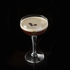 a close up of a drink in a wine glass on a black table with a dark background