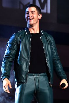 a male in a black shirt and green leather jacket is smiling at the camera while standing on stage