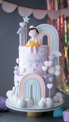 a pink and white cake decorated with rainbows, clouds, and a princess on top