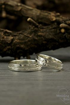 two wedding rings sitting next to each other on a wooden surface with driftwood in the background