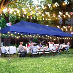 a group of people sitting at tables under a blue tent with lights strung from it