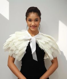 a woman with white wings and a black dress is posing for the camera in front of a white wall