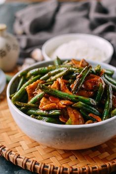 a white bowl filled with green beans and meat on top of a wooden tray next to rice