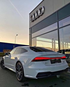 the rear end of a white car parked in front of an audi dealership at sunset