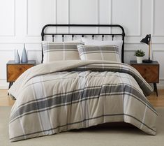 a bed with plaid comforter and pillows in a white room next to a wooden dresser