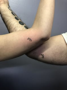 two men with matching tattoos on their arms, one is holding the other's arm