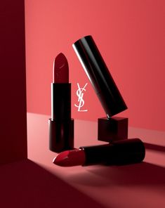 a red lipstick with the ysl logo on it is sitting in front of a pink background