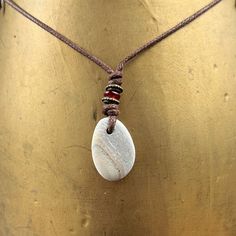 Beach pebble necklace, beige striped raw stone pendant, rock jewellery, brown cotton cord, beach found rock to wear I found this pebble on the beach in Cornwall and hung it on a brown cotton cord. The pebble is beige colour and has a faint stripes running through it I have drilled the pebble and hung it on a knotted adjustable natural coloured cotton cord  with a narrow red glass bead and two narrow bronze beads  The pebble measures approximately 27mm tall, 19mm wide and 5mm thick, the over all Beach Necklaces With Brown Natural Stones, Beach Necklace With Brown Natural Stones, Beach Brown Necklace With Natural Stones, Minimalist Waxed Cord Jewelry For Beach, Brown Pendant Jewelry For Beach, Brown Pendant Jewelry For The Beach, Brown Waxed Cord Beach Necklaces, Brown Waxed Cord Necklaces For The Beach, Handmade Cord Jewelry For The Beach