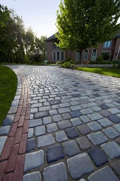 a cobblestone driveway with grass and trees in the background