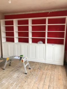 an empty room with red and white bookcases on the wall, two ladders in front of it