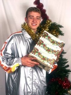 a man in silver pajamas holding up a cake with christmas decorations on it and a tree behind him