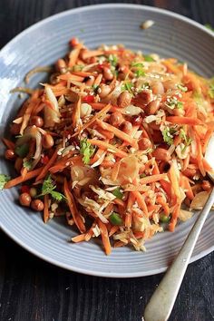 a white plate topped with carrots and nuts next to a spoon on a wooden table