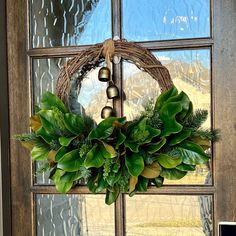 a wreath hanging on the front door of a house with bells and greenery around it