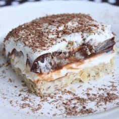 a piece of cake on a white plate with chocolate shavings and powdered sugar