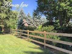 a wooden fence in the middle of a yard with trees and grass on both sides