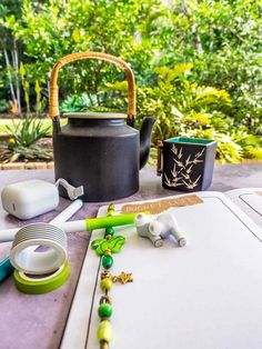 a tea pot and other items sitting on a table outside with trees in the background