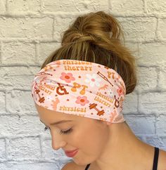 a woman wearing a pink headband with brown and white letters on it, in front of a brick wall