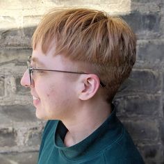 a young boy wearing glasses standing in front of a brick wall and looking off into the distance