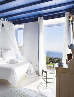 a white bed sitting under a blue ceiling in a bedroom next to a large window