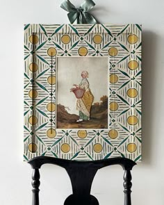 a painting hanging on the side of a wall next to a wooden chair with a bow