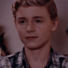 a close up of a young man wearing a plaid shirt and looking at the camera