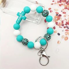 a blue and white beaded bracelet with a cross charm on the clasp is sitting next to some confetti