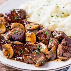 a white plate topped with meat and mushrooms next to mashed potatoes