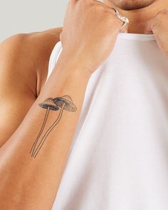 a man with a mushroom tattoo on his arm is looking at the camera while he adjusts his watch