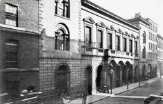 an old black and white photo of people standing on the sidewalk in front of a building