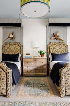 two beds in a bedroom with blue and white bedding, rugs and lamps