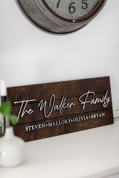 a wooden sign sitting on top of a white table next to a clock and vase