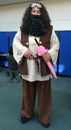 a man dressed in costume with long black hair and beard holding a pink rose while standing next to a blue wall