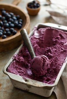 a scoop of purple ice cream in a pan with berries on the table behind it