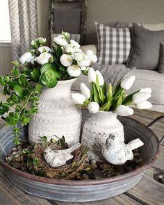 two white vases filled with flowers sitting on top of a table next to a couch