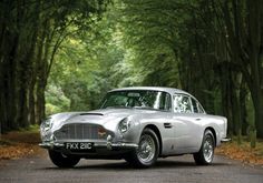 an old silver car is parked on the side of the road in front of some trees