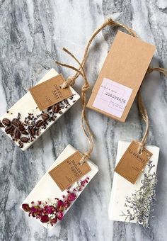 three soap bars with dried flowers on them sitting on a marble counter top next to tags