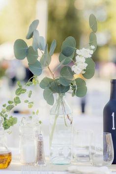 the table is set with glasses, bottles and flowers in vases that are on top of each other