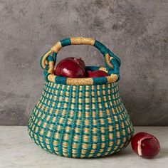 a green and yellow basket with an apple in it next to a red apple on the table